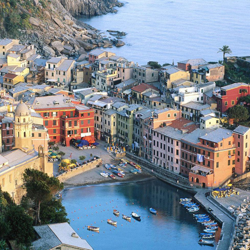 Aerial view of a colourful coastal village with boats moored in a sheltered cove